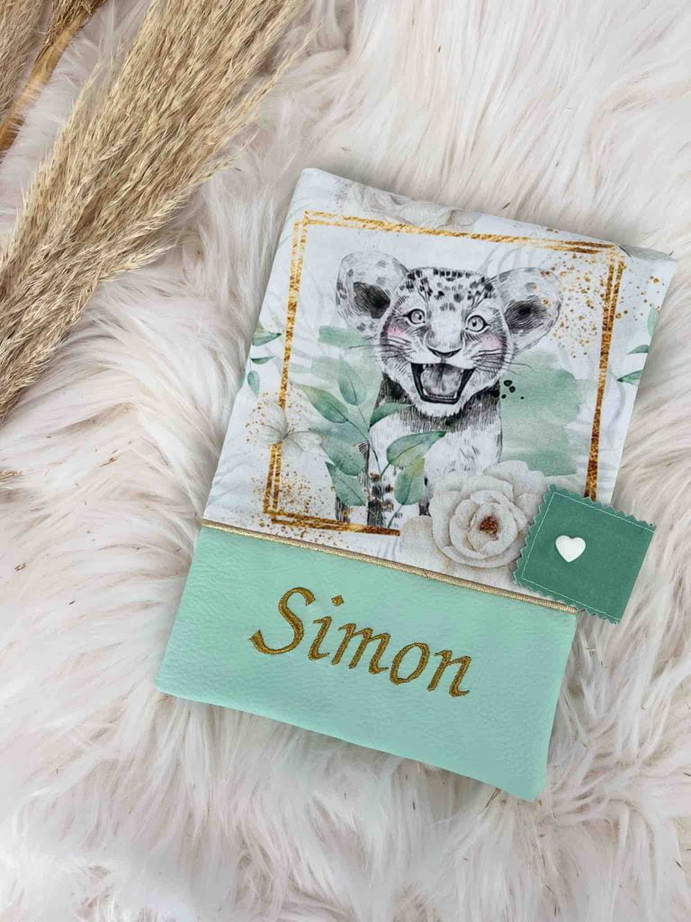 Exemple de protège carnet de santé à personnaliser de style savane, le bas de couleur vert d'eau, et le prénom Gabin de brodé en doré.