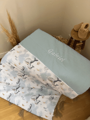 Couverture bébé personnalisée thème marin, cousue main en France avec un tissu exclusif créé par Jenni. Prénom brodé et couleur unie au choix. Cadeau de naissance unique, doux et rassurant.